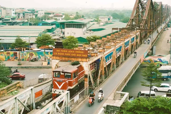 Elevated view of a first-class sleeper train in Vietnam traversing a graffiti-laden bridge, integrating travel with urban art.