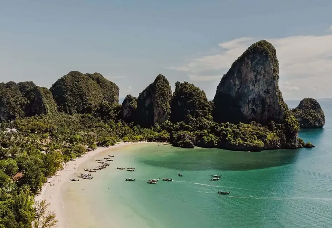 Railay Beach's stunning landscape, featuring a pristine sandy shore lined with longtail boats and framed by dramatic limestone cliffs, a breathtaking view on the journey from Ao Nang to Railay Beach.