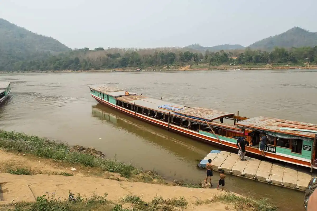 Several Laos slow boats moored at the river's edge, with passengers preparing to disembark in Luang Prabang.