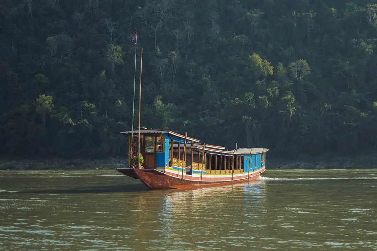 A 'slow boat to Luang Prabang' elegantly glides along the Mekong River, surrounded by dense tropical forest