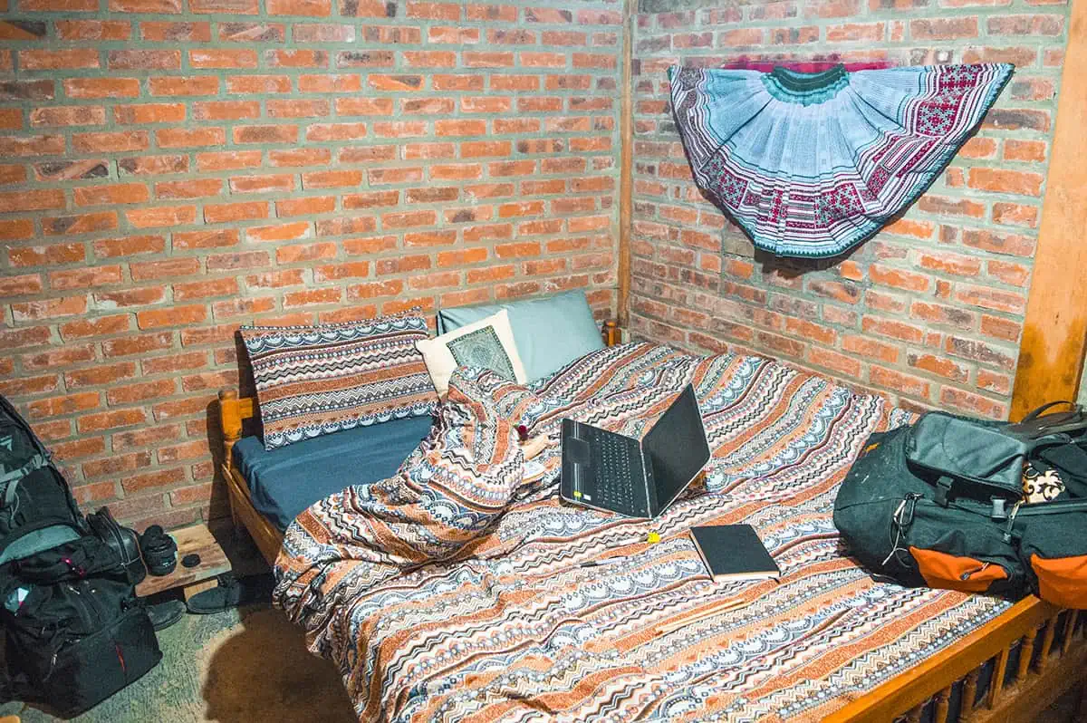 Bed with colorful bedding and a laptop in a room with exposed brick walls at our homestay in Sapa.