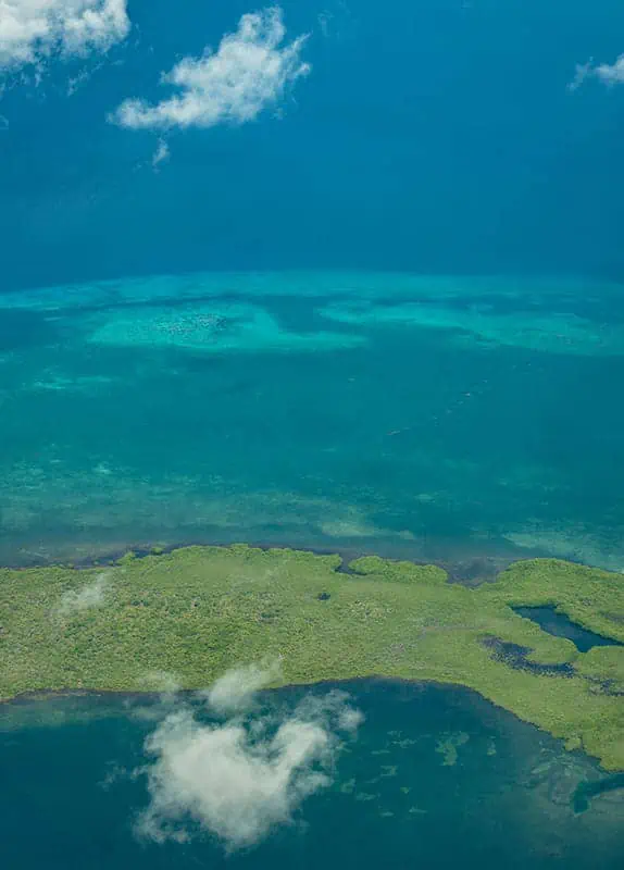 Belize In June: Is Belize Worth Visiting In June? 57 Aerial view of the Belize Barrier Reef with patches of coral and a small island, illustrating the stunning natural beauty accessible in June.