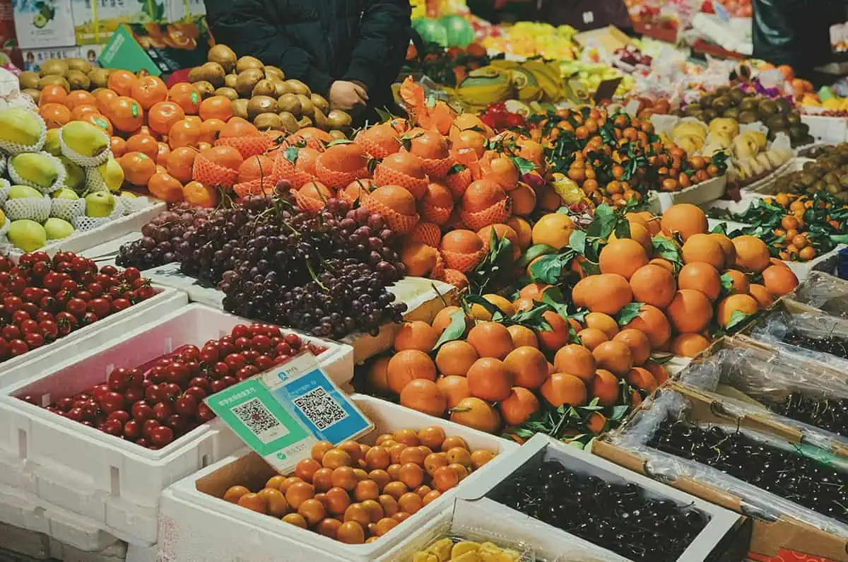 Fruits In Belize: The BEST 24 Fruits Worth Trying On Your Visit 4 A vibrant array of fruits for sale at a market, featuring oranges, kiwis, grapes, and strawberries, showcasing the diversity of fruits in Belize.