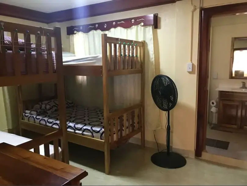 Best Hostels In San Ignacio: 5 Excellent Stays For Travelers On A Budget 60 Cozy and well-maintained dormitory room with wooden bunk beds and a standing fan, at D's Hostel, one of San Ignacio's comfortable accommodations.