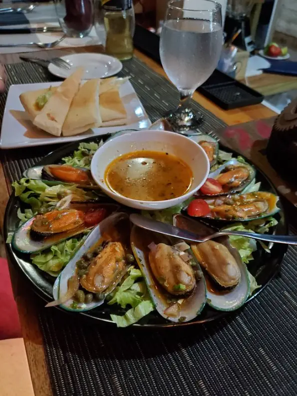 12 Best Restaurants In San Ignacio: Top Eats For Visitors 63 A tantalizing plate of mussels in a garlic broth with fresh greens and toasted bread on the side from crave house of flavors, a must-try dish in San Ignacio's dining scene.