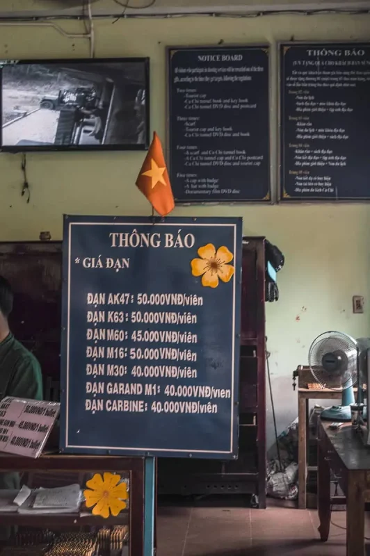 Best Cu Chi Tunnels Tours: Cheap VS Expensive 2026 53 Interior of a Cu Chi site displaying a board with prices for firing various guns, like AK47 and M16, reflecting the historical military aspect of the tunnels.