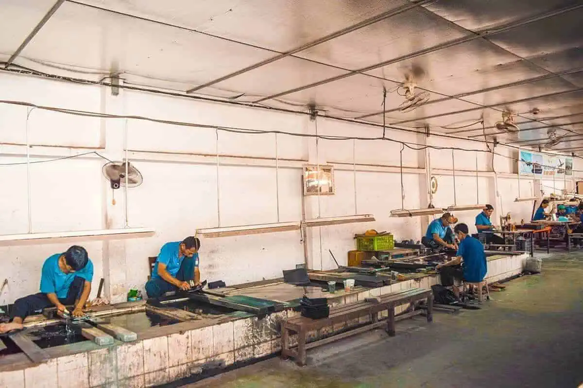 Best Cu Chi Tunnels Tours: Cheap VS Expensive 2026 46 Workers in blue uniforms at the lacquer stop off during the cu chi tunnels tour demonstrating manufacturing processes.