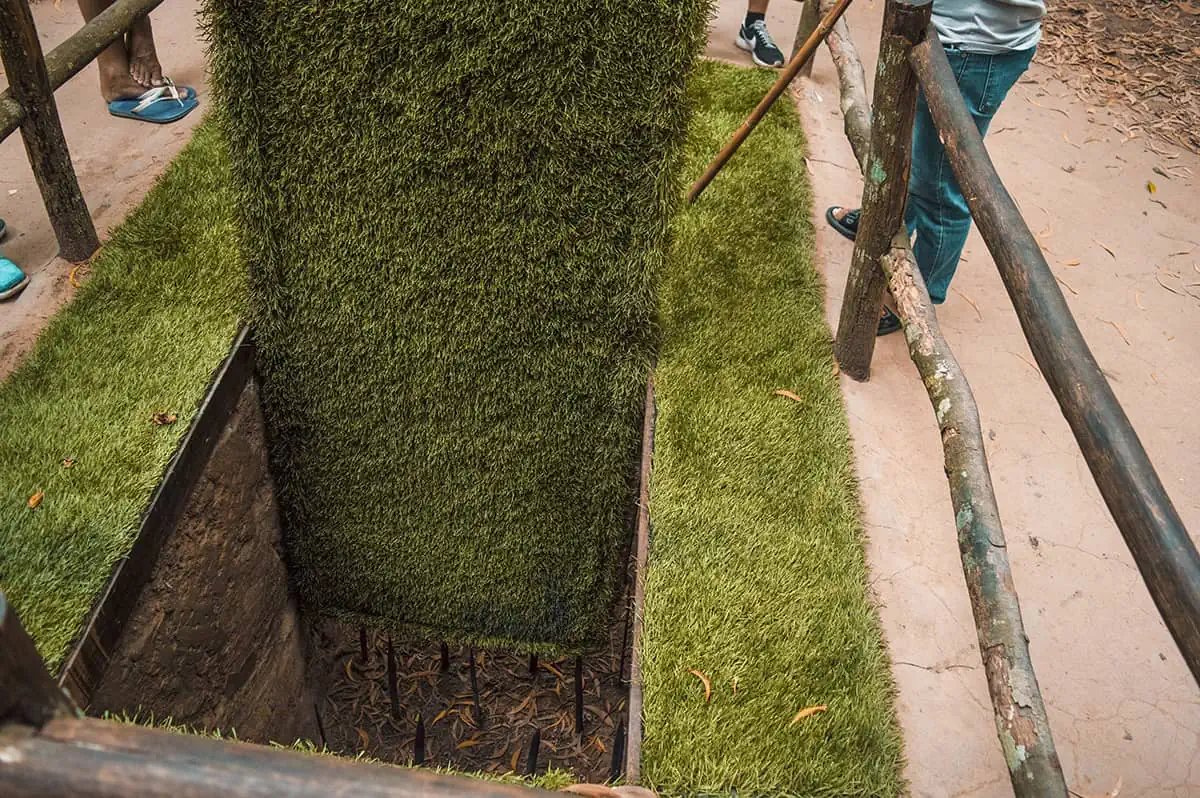 Best Cu Chi Tunnels Tours: Cheap VS Expensive 2026 54 A close-up view of a booby trap at the Cu Chi Tunnels, with sharp spikes at the bottom of a deep pit, surrounded by artificial grass to illustrate how traps were hidden during wartime.