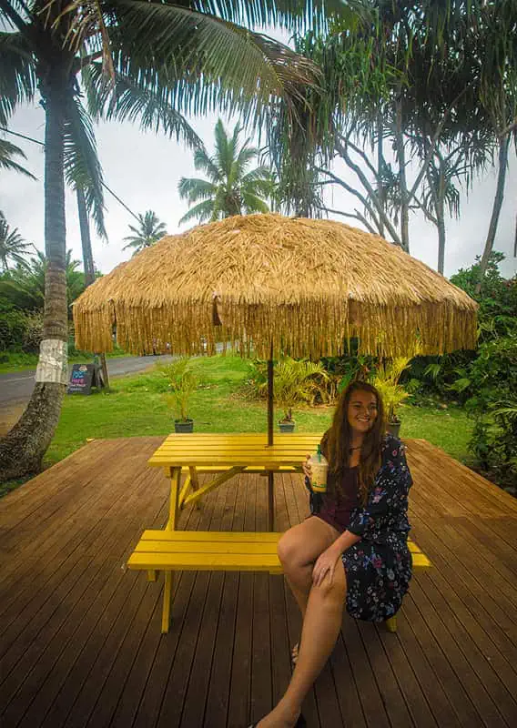 Where To Eat In Rarotonga: BEST Restaurants & Cafes 2026 23 tasha amy enjoying a leisurely break under a thatched umbrella at a scenic outdoor seating area, typical of the best restaurants in Rarotonga.