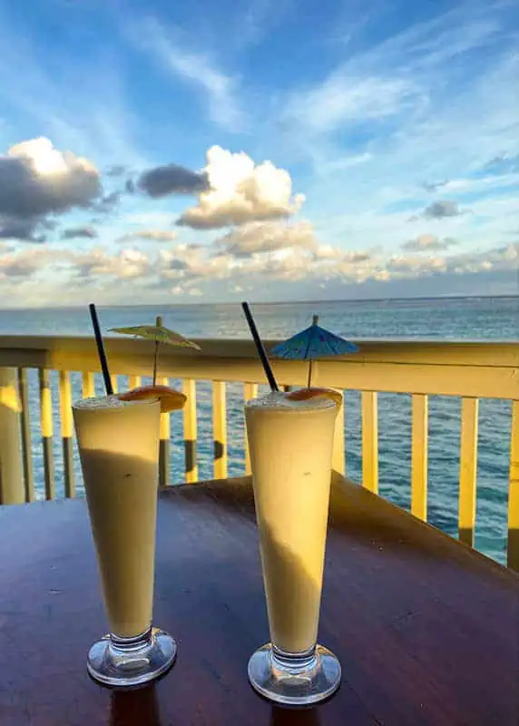 Where To Eat In Rarotonga: BEST Restaurants & Cafes 2026 39 Two creamy pina coladas with decorative umbrellas against a seaside backdrop, served at captain andys bar and grill at the rarotongan