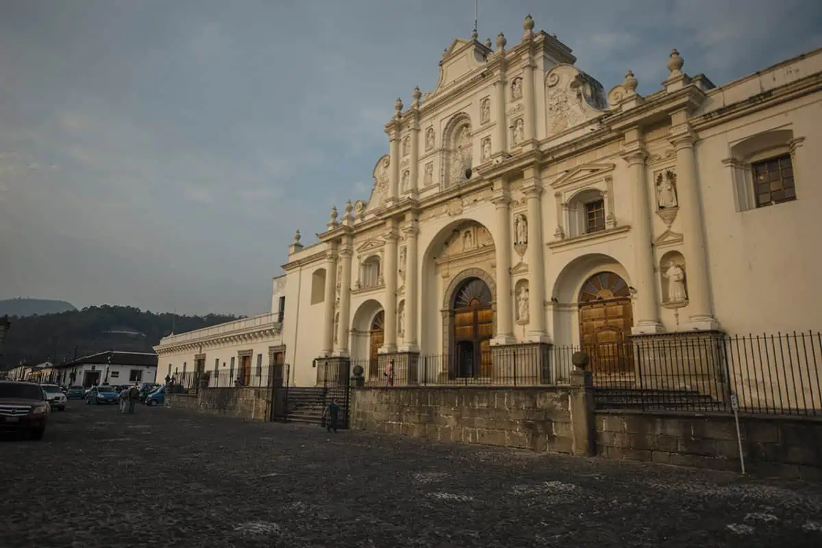 Mexico Belize Guatemala Itinerary: BEST Backpacking Route 111 The historic Cathedral of Antigua, Guatemala, captured in the early evening with a muted sky in the background. The church's elaborate white facade features intricate sculptural details and classical architectural elements. The scene is set on a cobblestone street, enhancing the old-world charm of this colonial city.