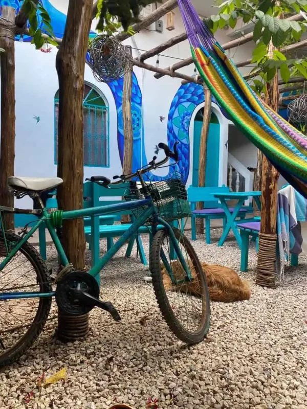 Mexico Belize Guatemala Itinerary: BEST Backpacking Route 101 A vibrant and artistic courtyard in Flores featuring a green bicycle parked on a gravel ground, colorful hammocks, and a large mural of a blue octopus on the wall. The scene is embellished with various hanging decorations and plants, creating a lively and welcoming atmosphere.