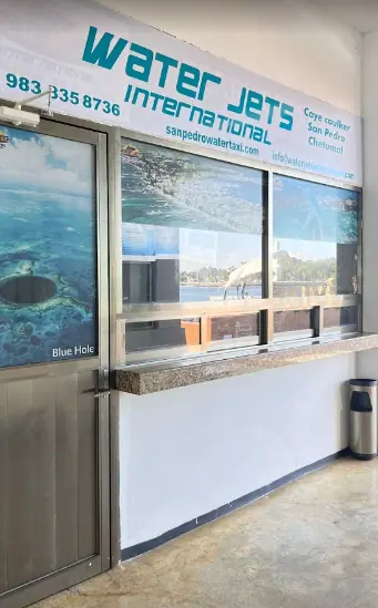 Bacalar To Caye Caulker: The ULTIMATE Travel Guide 2026 56 The Water Jets International ticket office, providing ferry services to Caye Caulker, San Pedro, and Chetumal. The office features a sign with contact details and a promotional image of the Blue Hole.