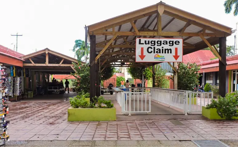 Bacalar To Caye Caulker: The ULTIMATE Travel Guide 2026 61 Small luggage claim area at the belize water taxi terminal. The area is surrounded by greenery and rustic buildings.