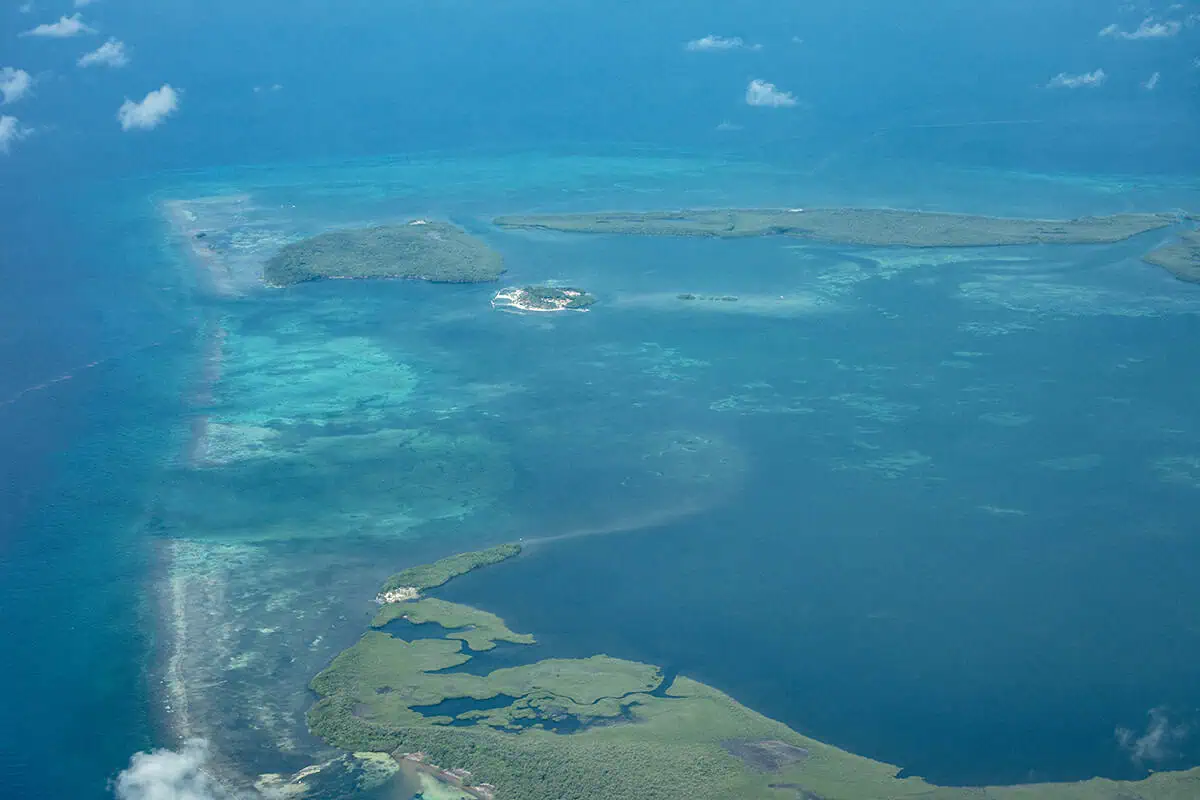 The 31 BEST Things To Do In Caye Caulker: Ultimate List! 56 A panoramic aerial view of the Belize Barrier Reef near Caye Caulker, featuring an expanse of azure ocean dotted with small, lush islands and coral formations. The various shades of blue and green in the water indicate the depth and diversity of the marine ecosystem. seeing the great blue hole is one of the best things to do in caye caulker
