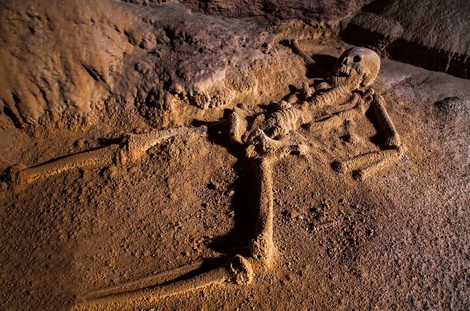 Best Things To Do In San Ignacio: Caves, Ruins & Day Trips 57 Close-up of an ancient skeleton lying on the sandy ground inside a cave. The bones are partially covered in dust, emphasizing the archaeological significance and the historical explorations that can be undertaken in the caves of San Ignacio.