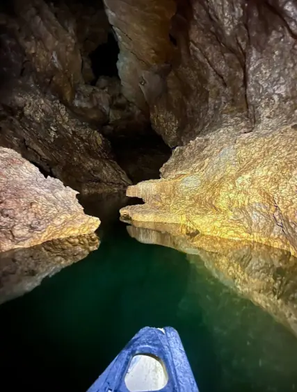 Best Things To Do In San Ignacio: Caves, Ruins & Day Trips 74 Inside a narrow cave passage with clear, emerald-green water. The rocky walls of the cave are illuminated, showcasing the textures and formations, and emphasizing the exciting caving and exploration opportunities available in San Ignacio