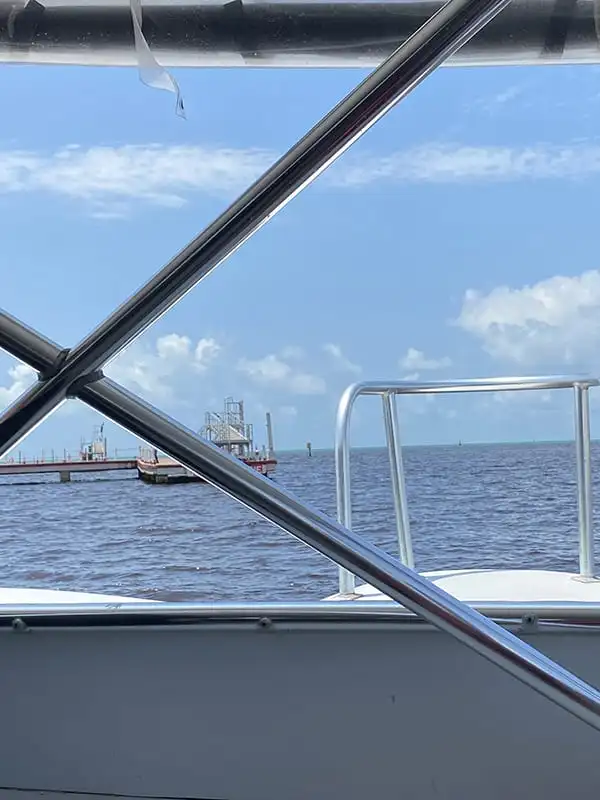 Chetumal To Caye Caulker: Best & Easiest Transport 2026 56 The ocean through the window of a ferry as it departs from Chetumal. The ferry heads across the water, with an industrial port in the distance.