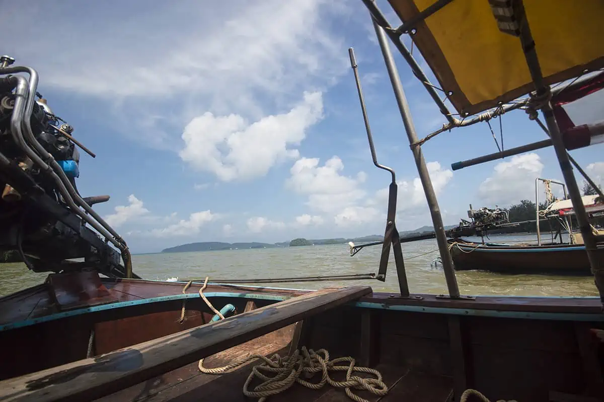 Is Railay Beach Closed: What You Need To Know (2026) 54 View from a long-tail boat on Railay Beach, showing the engine, a coiled rope, and the expansive sea under a bright blue sky with scattered clouds. This image suggests boating activities are ongoing, posing the question: "Is Railay Beach closed?"