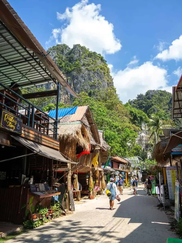 Is Railay Beach Closed: What You Need To Know (2026) 51 Lively street scene at Railay Beach with tourists walking past shops and cafes, set against the backdrop of lush green hills and a clear blue sky.