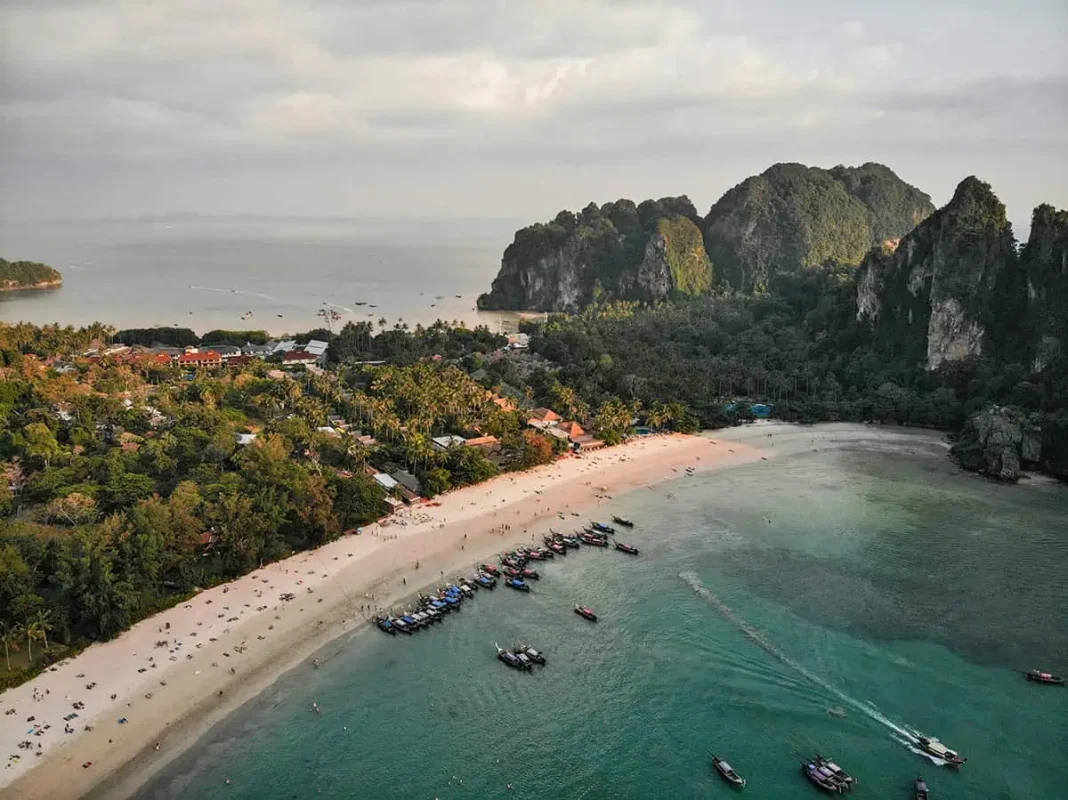 Is Railay Beach Closed: What You Need To Know (2026) 53 Aerial view of Railay Beach with sandy shores, numerous boats docked near the water, and lush greenery surrounding the area under a bright sky.