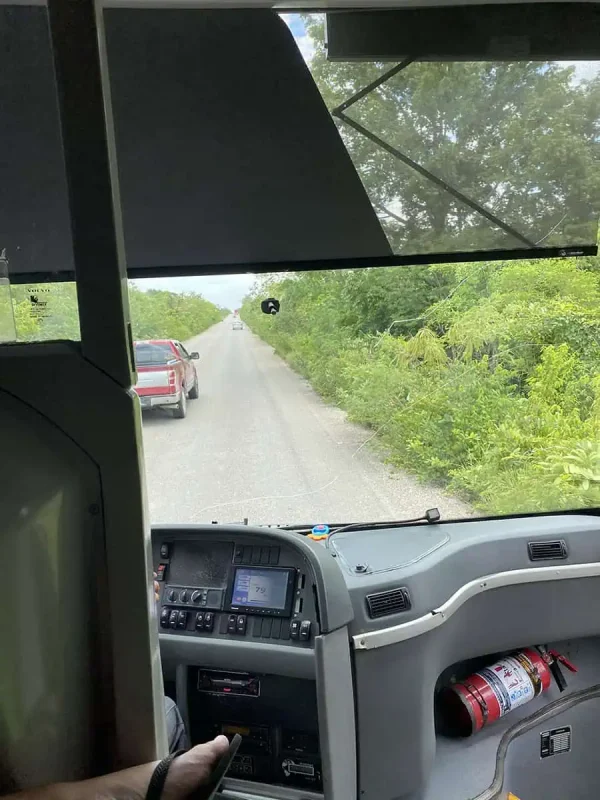 Mexico And Belize Itinerary: From 2 to 5 Weeks 62 View from inside a bus traveling on a rural road flanked by lush green vegetation. The bus dashboard is visible, and a red car can be seen ahead on the road, highlighting the journey through Mexico and Belize.