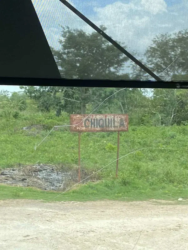 Mexico And Belize Itinerary: From 2 to 5 Weeks 63 A rusty sign reading "Chiquila" partially obscured by greenery, seen through a bus window, marking a point of interest on a Mexico and Belize itinerary.