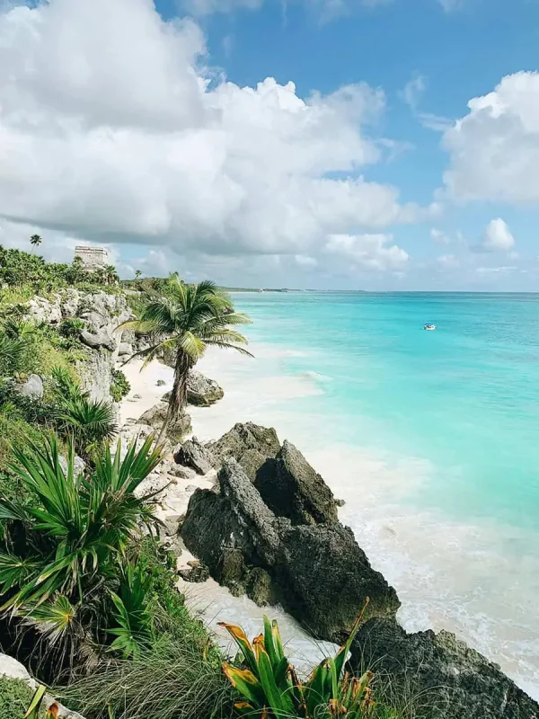 Mexico And Belize Itinerary: From 2 to 5 Weeks 72 Stunning beach scene in Tulum, Mexico, with clear turquoise waters gently lapping against the white sandy shore. Large rocks and lush greenery add to the picturesque setting, with a historic Mayan structure visible on the cliff, a must-visit on a Mexico and Belize itinerary.