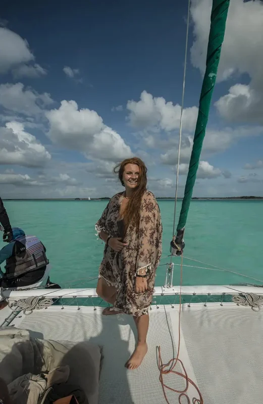 Mexico And Belize Itinerary: From 2 to 5 Weeks 84 Tasha Amy standing on the deck of a sailboat with turquoise waters and a cloudy sky in the background. She is smiling and holding onto the boat's rigging, enjoying the breeze and the scenic beauty, embodying the joy and excitement of a Mexico and Belize itinerary.