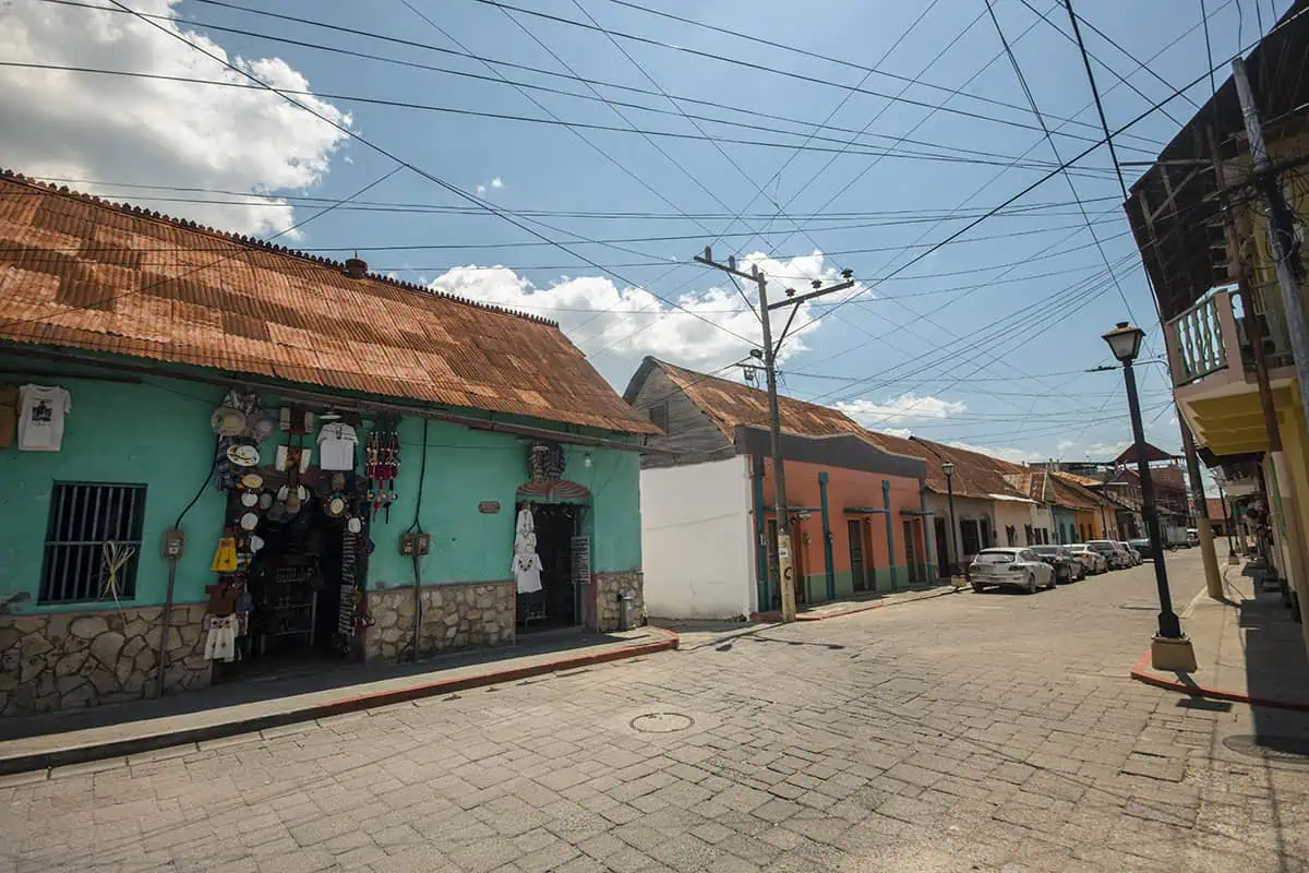 Another view of Flores, this time showing a different cobblestone street with a few shops and houses under a clear blue sky. The wires crisscrossing above add a touch of everyday life.