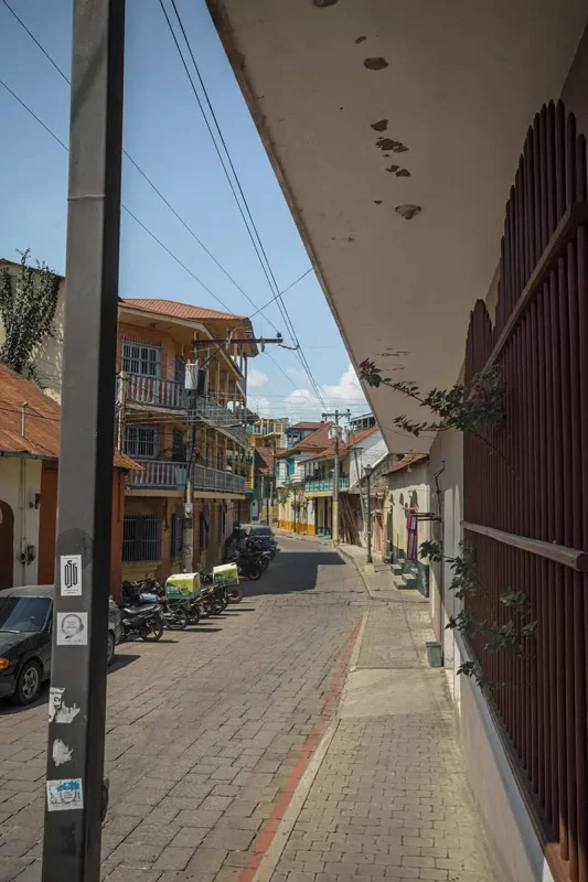 A narrow street in Flores, showcasing tightly packed houses with balconies and motorbikes parked along the sides. This scene represents the bustling yet charming streets of Flores.