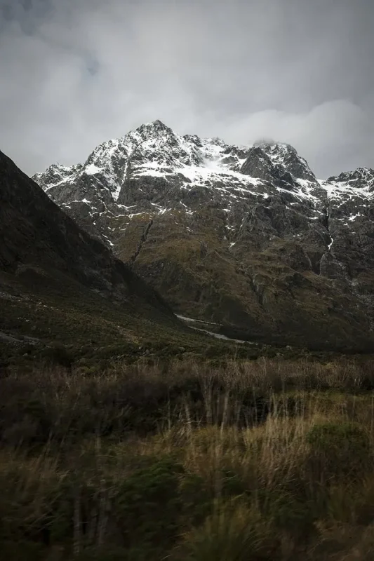 Milford Sound In Winter: Is It Still Worth The Hype? 25 A close-up view of a rugged, snow-capped mountain peak against a cloudy sky. The steep, rocky slopes and patches of snow highlight the raw and awe-inspiring natural beauty typical of winter in Milford Sound.