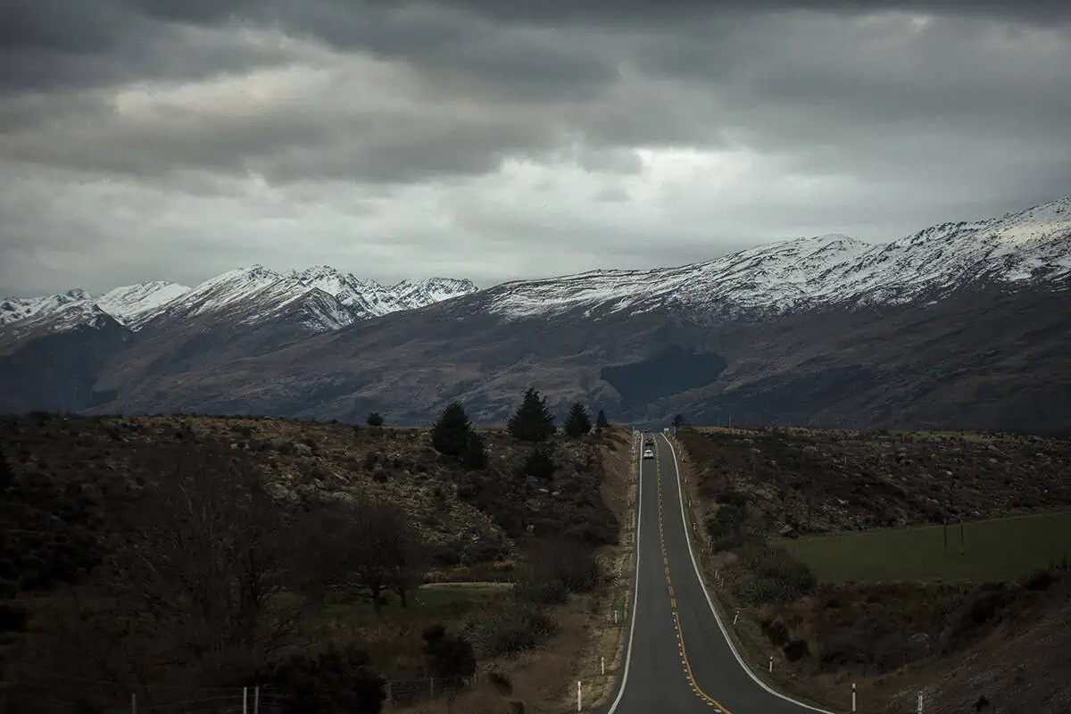 Fiordland & Milford Sound Lord Of The Rings Locations (2026) 23 A long straight road leads into a valley of rugged mountains dusted with snow in fiordland