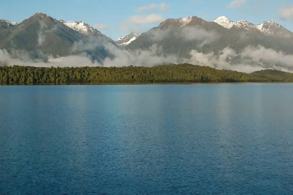 Fiordland & Milford Sound Lord Of The Rings Locations (2026) 21 Calm waters stretch before a line of forest and mountains partly covered in mist at Manapouri Lake
