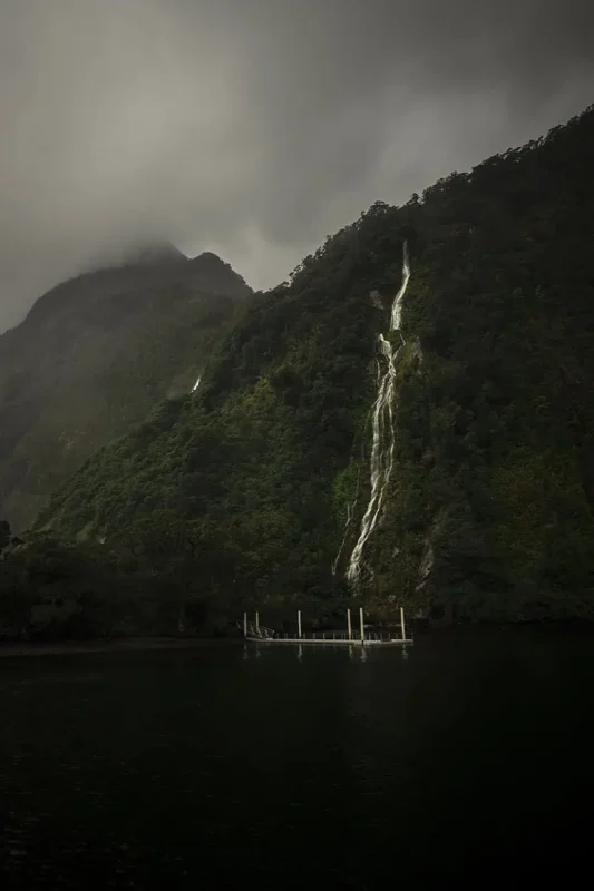 A tall and narrow waterfall running down steep cliffs into the waters of Milford Sound.