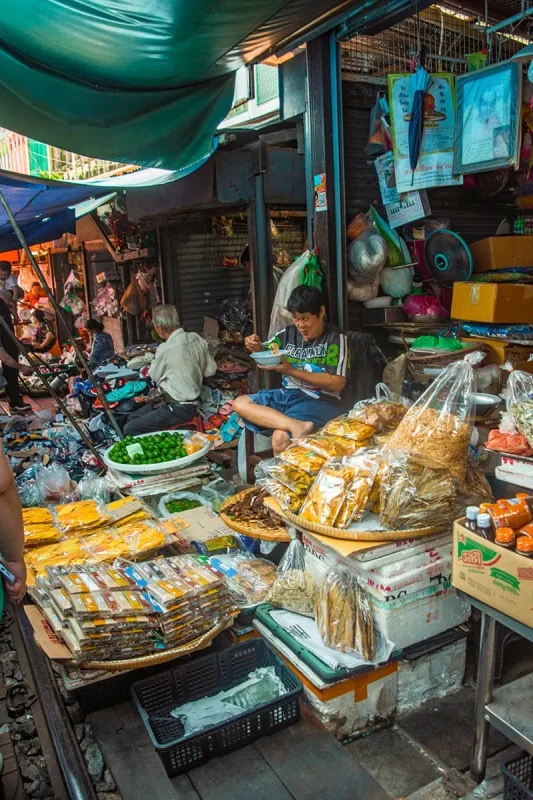 2 Days in Bangkok Itinerary For First-Time Visitors 55 a man sitting at his stall at the Maeklong Railway Market in Bangkok selling snacks and spices