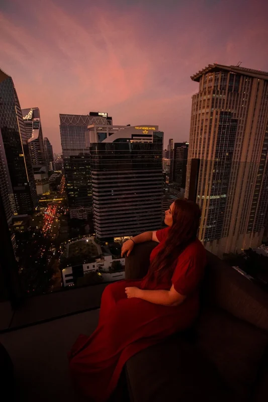 2 Days in Bangkok Itinerary For First-Time Visitors 49 Tasha Amy sitting in the corner of CHAR Sky Bar in Bangkok with traffic below as the sunsets