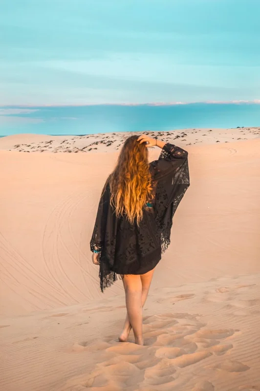 3 Weeks In Vietnam Itinerary: The Perfect First-Time Route 87 Tasha Amy in a black shawl walking on the white sand dunes with footsteps behind her in Mui Ne, Vietnam