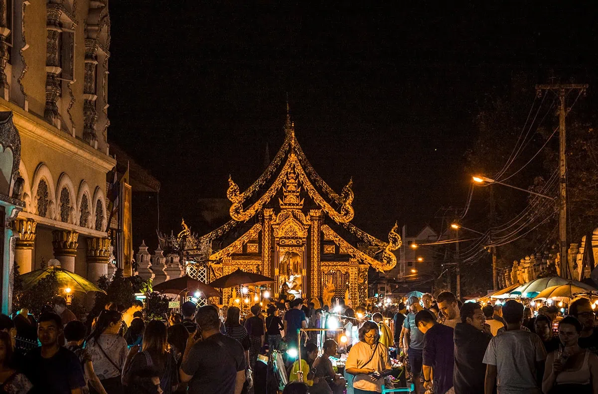 Night time view of a temple illuminated at the Chiang Mai Sunday market with crowds in front.