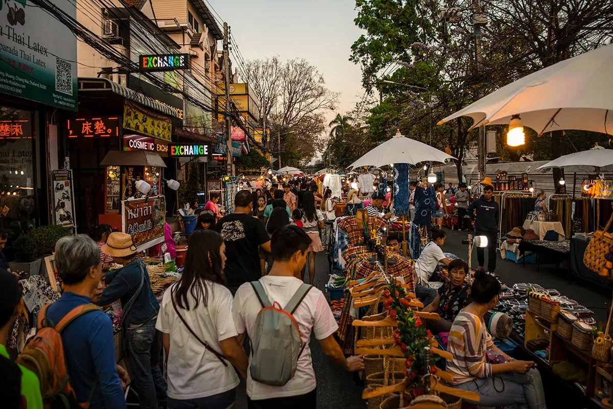 Shoppers and vendors on a busy street with stalls offering a variety of goods during golden hour in Chiang Mai during the Sunday Market