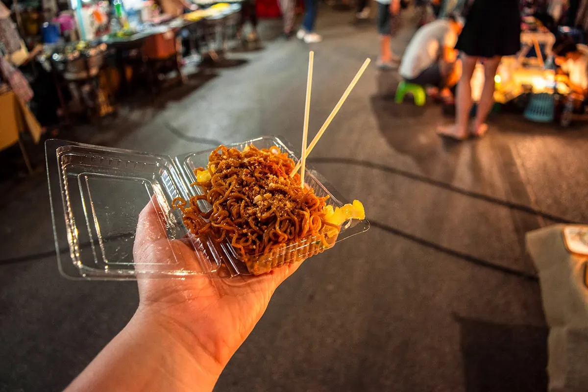 Tasha Amy with a helping of savory noodles packed in a clear takeaway container at the Sunday Night Market in Chiang Mai, Thailand