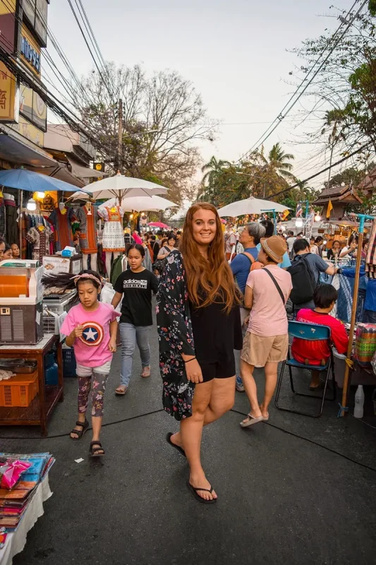 Tasha Amy smiling as she walks through the bustling lanes of the Sunday Market in Chiang Mai, Thailand surrounded by market stalls