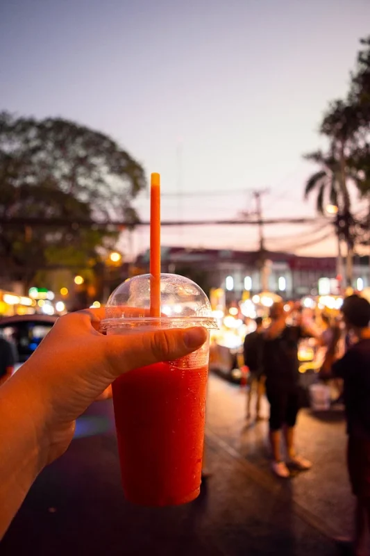Tasha Amy holding a a strawberry smoothie with crowds in the background at the Sunday Market in Chiang Mai