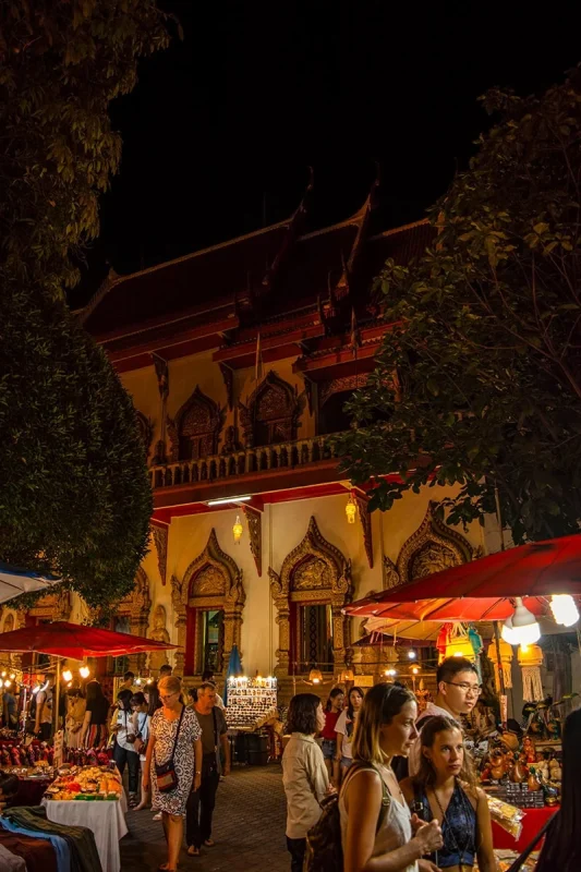 Crowds shopping market stalls with a temple in the background at the Chiang Mai Walking Street Market