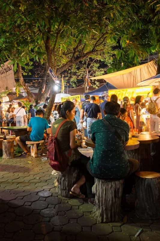 Patrons enjoying street food under trees at the Sunday market in Chiang Mai