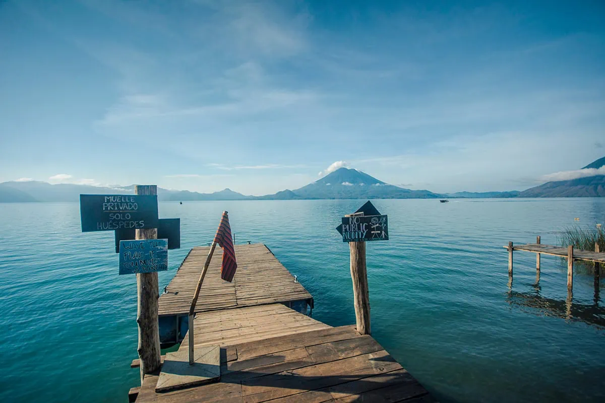 How To Get Around Lake Atitlan: Lanchas, Prices & Tips 24 The Free Cerveza Hostel pier with signs and a flag hanging around Lake Atitlan
