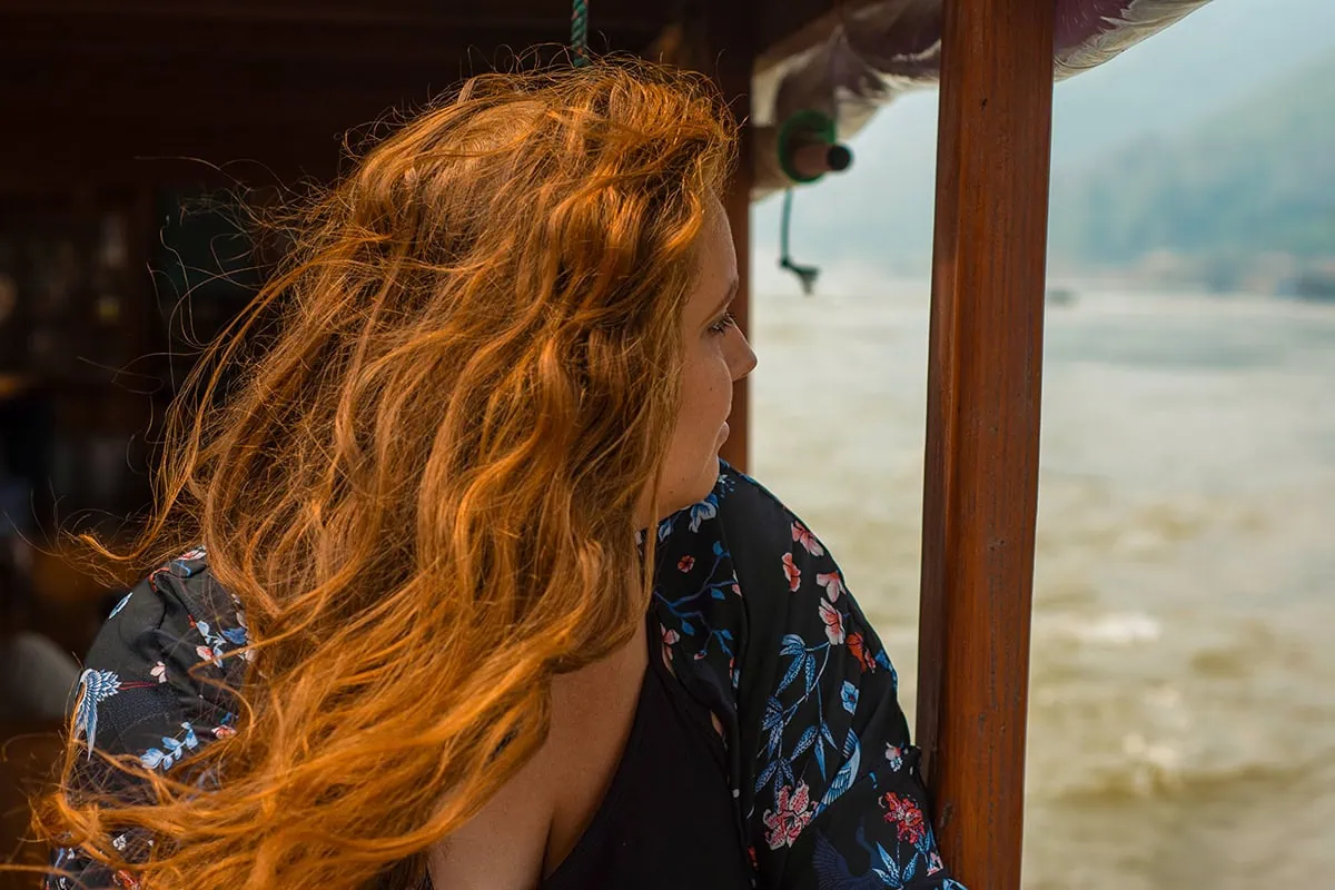 Slow Boat Laos: My Honest Guide After Doing It Twice (2026) 53 Tasha Amy with red hair gazes out from the shelter of a slow boat to Laos