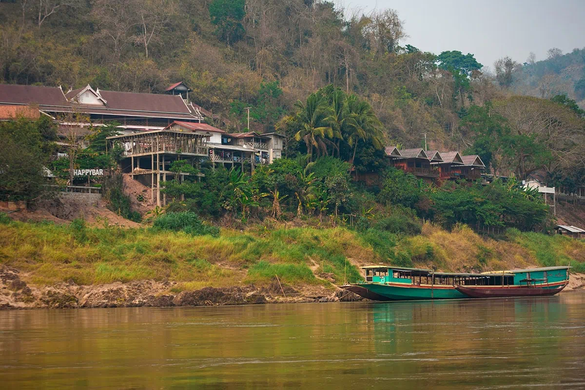 Slow Boat Laos: My Honest Guide After Doing It Twice (2026) 31 Looking out over the Mekong River across to the beginning of Pakbeng township in Laos with houses perched on the cliffside