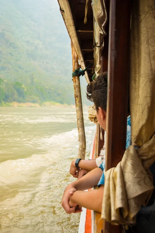 Slow Boat Laos: My Honest Guide After Doing It Twice (2026) 29 A man looks out from the side of the slow boat over the Mekong River