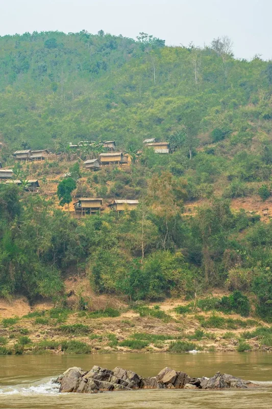 Slow Boat Laos: My Honest Guide After Doing It Twice (2026) 42 View from the slow boat looking up over the Mekong River to a small village perched on the hillside